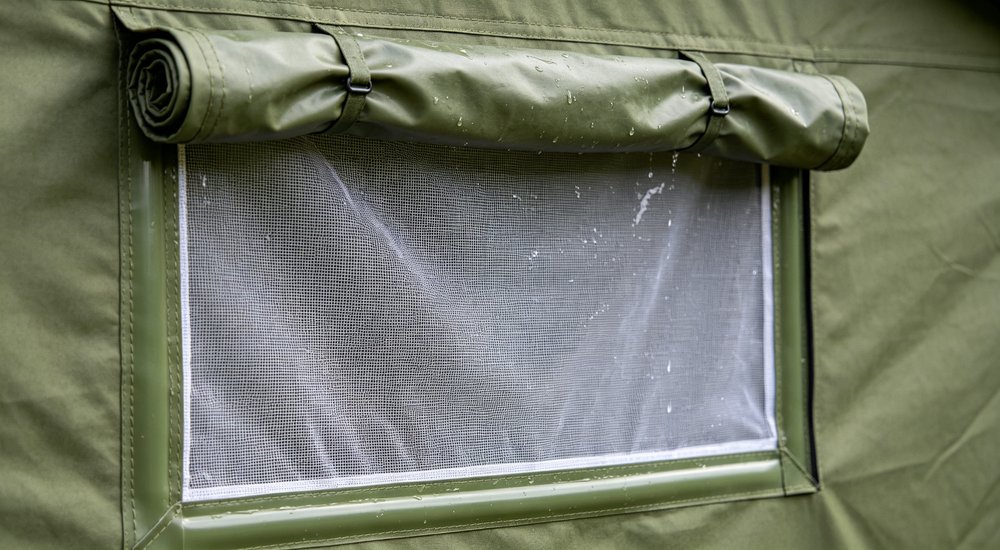 Close-up detail of green relief tent mesh window with integrated rain flap cover, insect screen netting and waterproof fabric flap design visible showing ventilation and rain protection dual function for tropical weather shelters