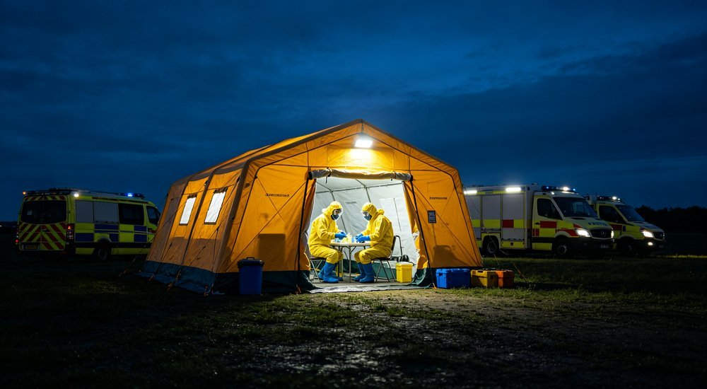 Wide angle shot of decontamination tent at night with emergency lighting and hazmat team working under dark blue sky during professional response