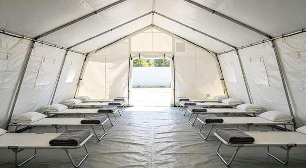 Interior of large white emergency shelter tent with folding beds, no people, custom OEM interior layout for displaced persons, professional product photography