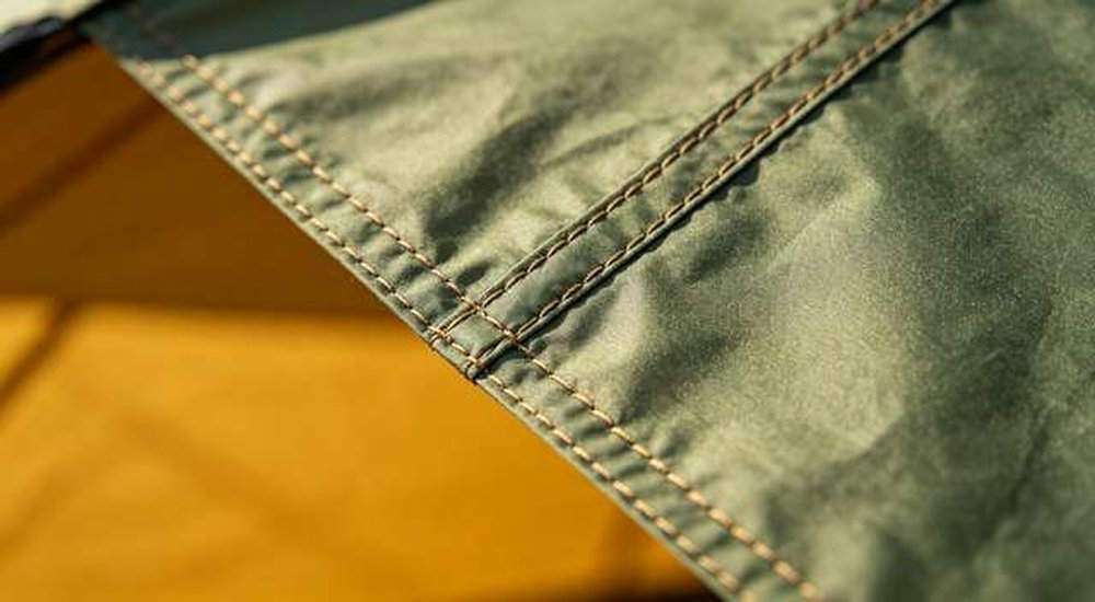 Close-up of tent fabric stitching and seam sealing detail, professional OEM manufacturing standards for emergency shelters, professional product photography, blue sky background
